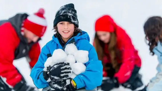 Boy in blue ski jacket holding a big pile of snowballs