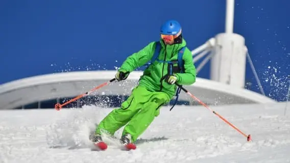 Man in green ski suit and blue helmet making a sharp left turn on crisp snow