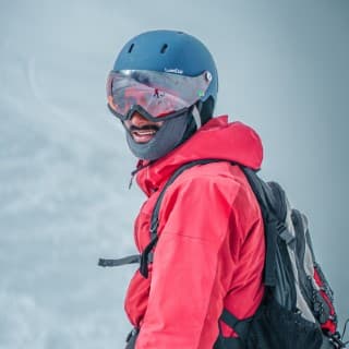 Man in red ski jacket and blue helmet standing in the snow