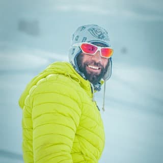 Man wearing yellow jacket, wooly hat and red snow glasses.