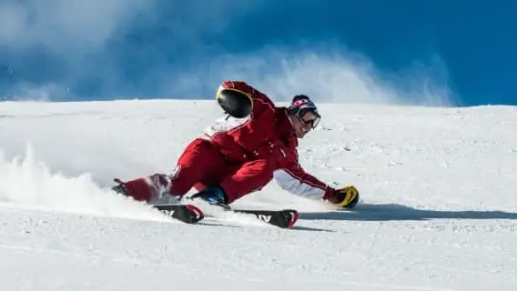 Man in red ski suit making a sharp turn on the slope with no ski poles