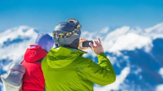 two people with their back to the camera taking a photo of snowy mountains